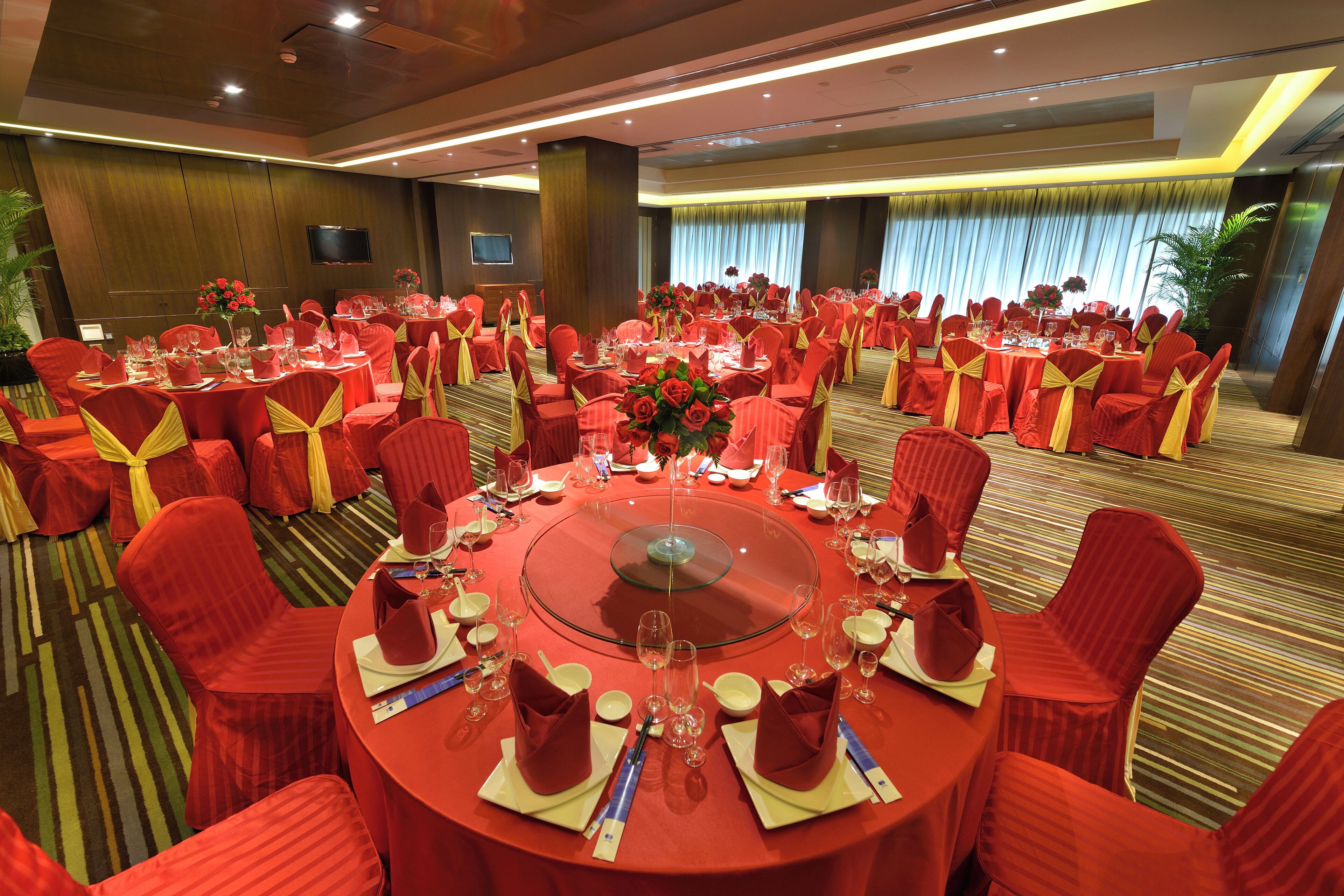A banquet hall with round tables, red chairs, and yellow sashes.