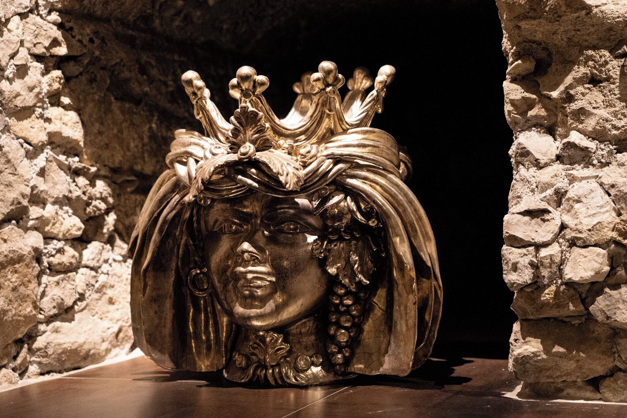 Eine goldene Krone mit filigranen Verzierungen vor einer Mauer aus Stein.