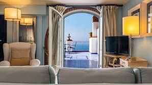 A hotel room with a balcony, a sofa, a television, and a lamp. - HOTEL VILLA CARLOTTA (Taormina)