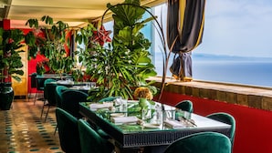 A restaurant with a view of the sea, green chairs, and large potted plants. - HOTEL VILLA CARLOTTA (Taormina)