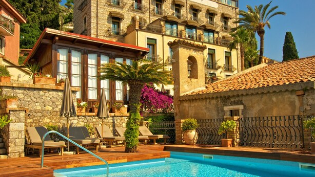 A pool area with lounge chairs, a stone building with balconies, and a clear blue sky. - HOTEL VILLA CARLOTTA (Taormina)