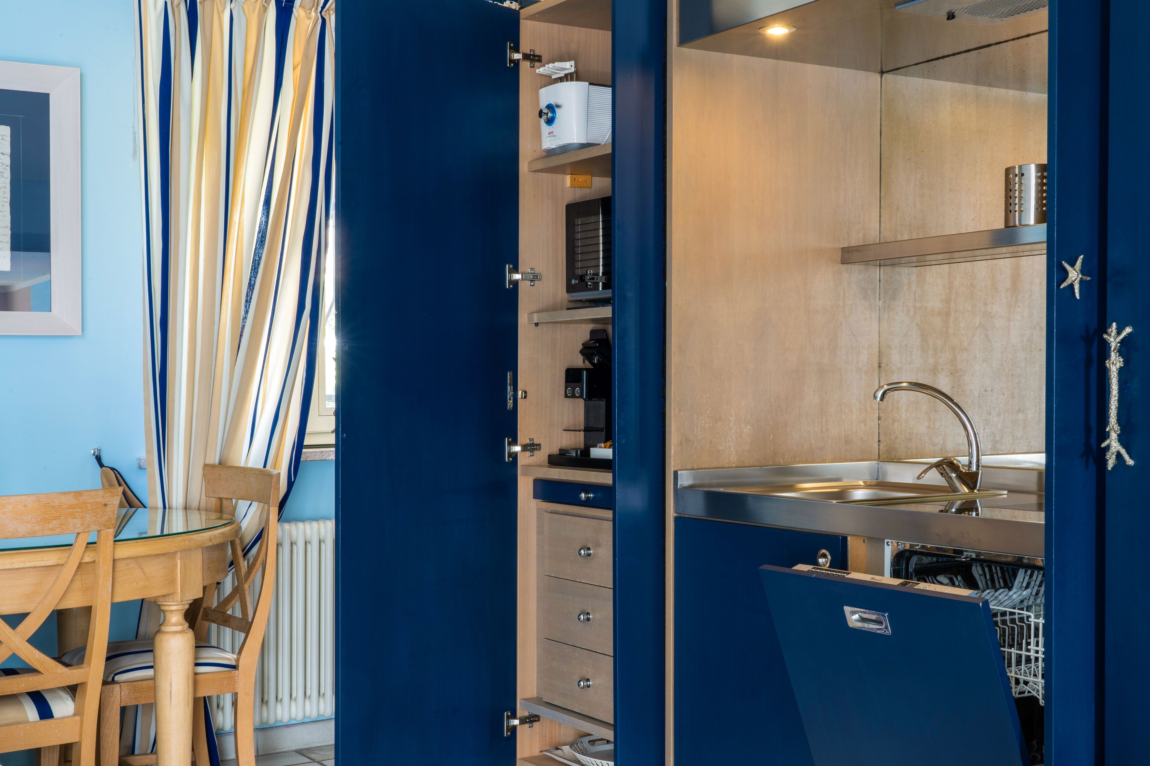 A compact kitchen with a built-in dishwasher, a sink, and a window with striped curtains.