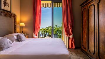 A hotel room with a bed, a nightstand, a lamp, a wardrobe, and a view of the outdoors.