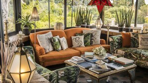 A cozy living room with a large window, a sofa, a coffee table with books, and decorative plants. - HOTEL VILLA CARLOTTA (Taormina)