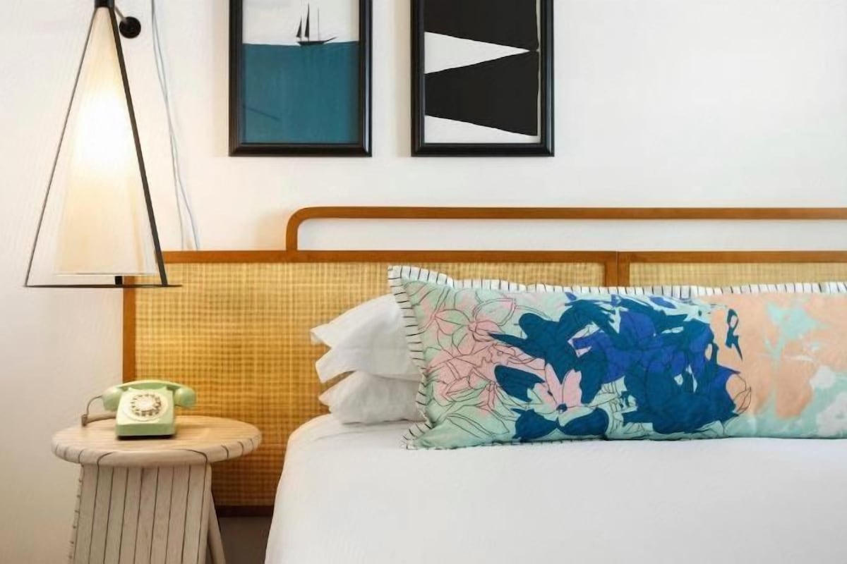 Una habitación de hotel con una cama, una lámpara de noche, un teléfono y una pared decorada con cuadros.