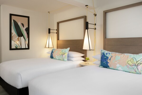 Habitación de hotel con dos camas, cada una con una almohada, una mesita de noche y una obra de arte colgada en la pared.