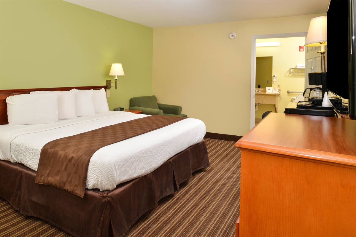 A hotel room with a large bed, a desk, a chair, and a bathroom visible through an open door.