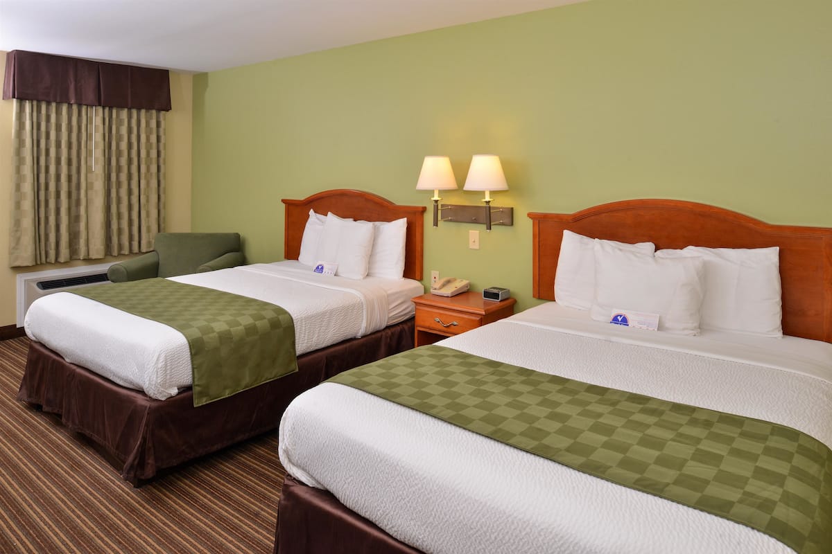 A hotel room with two beds, a desk, a chair, a lamp, and a window with curtains.