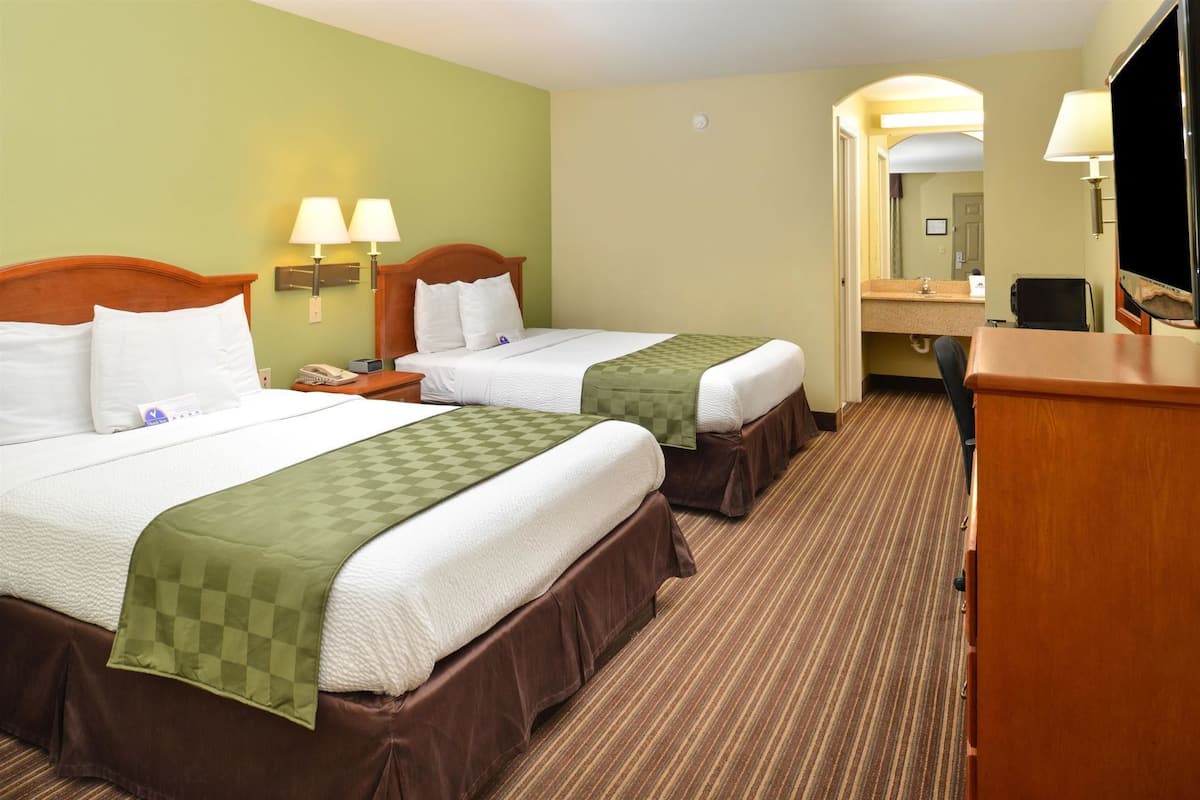 A hotel room with two beds, a desk, a chair, a mirror, and two wall-mounted lamps.