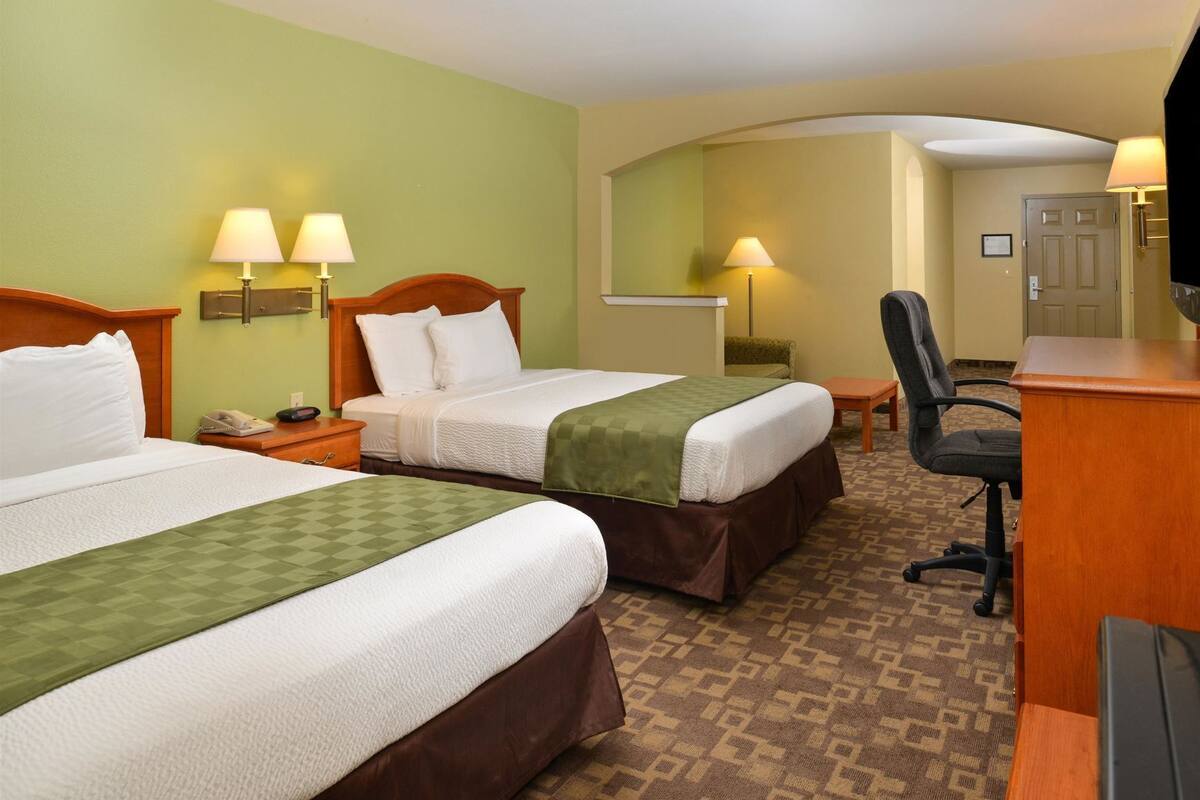 A hotel room with two beds, a desk, a chair, and a television.