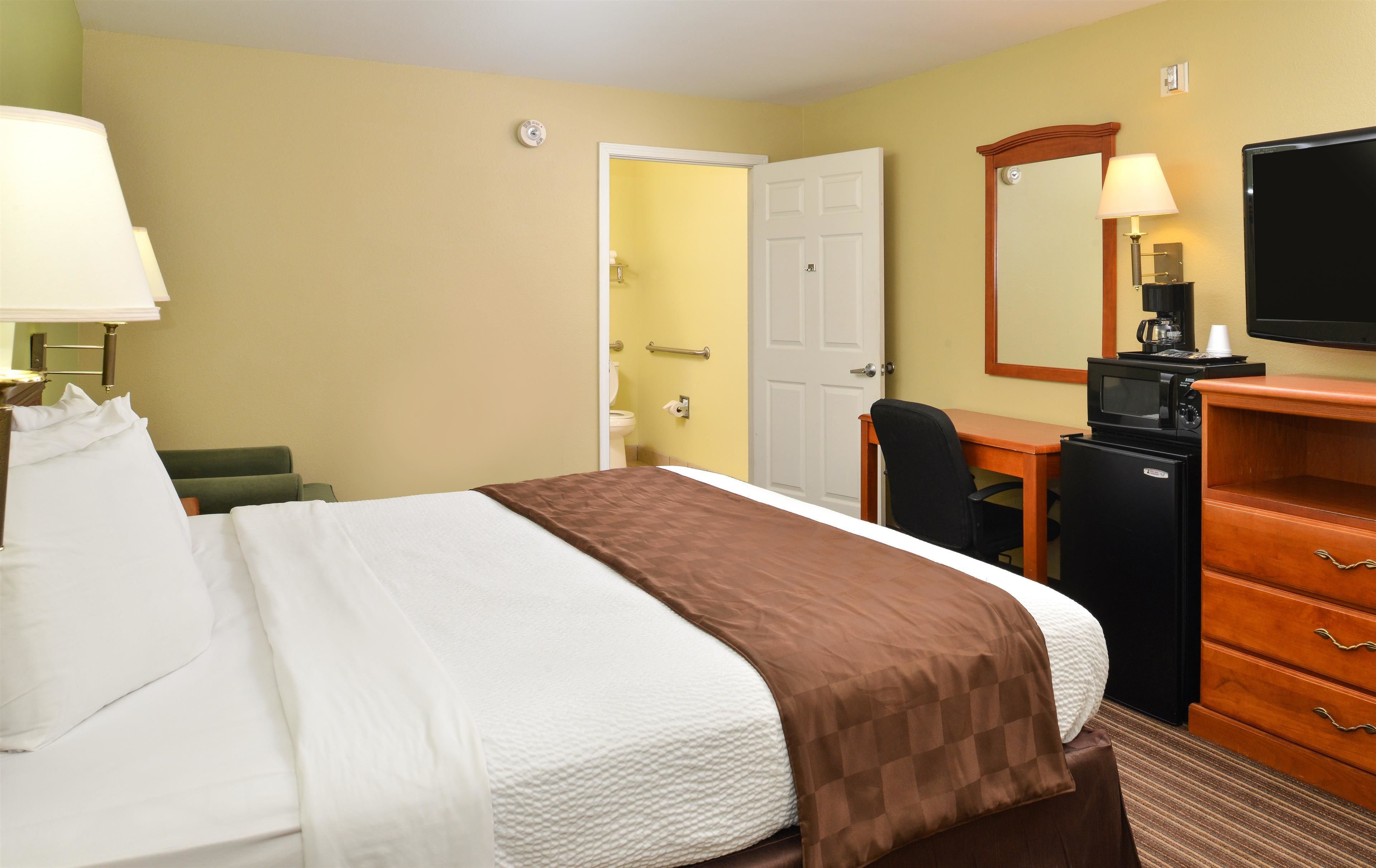 A hotel room with a bed, a desk, a chair, a dresser, a television, and a bathroom visible through an open door.