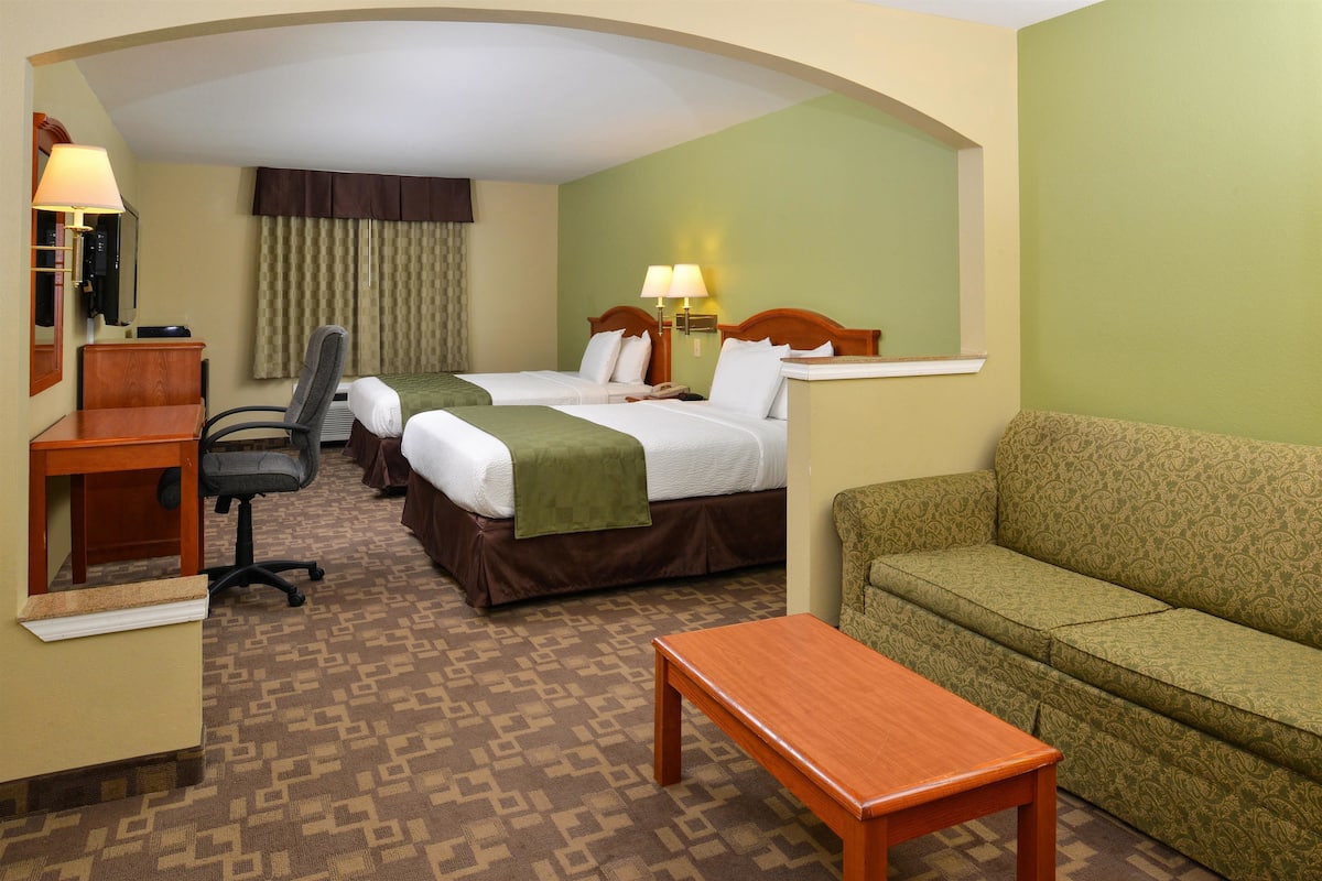 A hotel room with two beds, a desk, a chair, a sofa, and a small table.