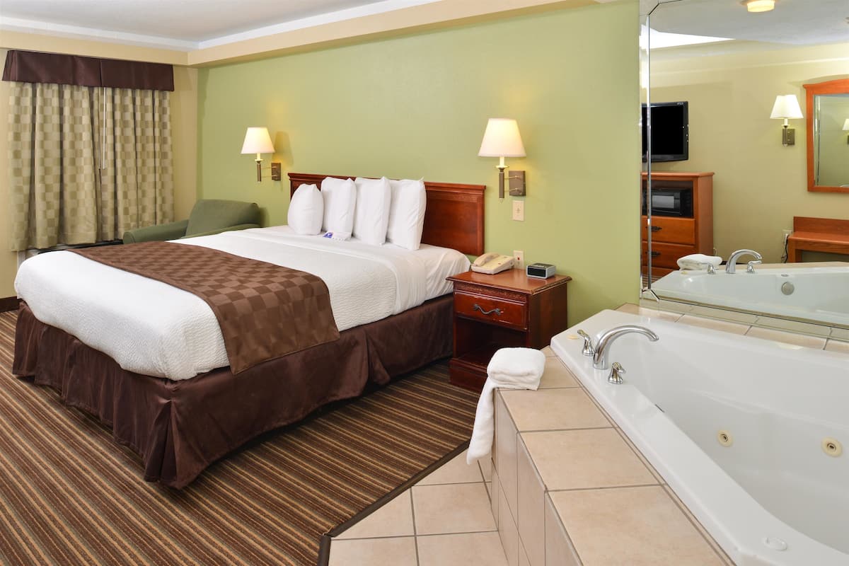 A hotel room with a large bed, a separate bathroom with a bathtub, and a television in the corner.