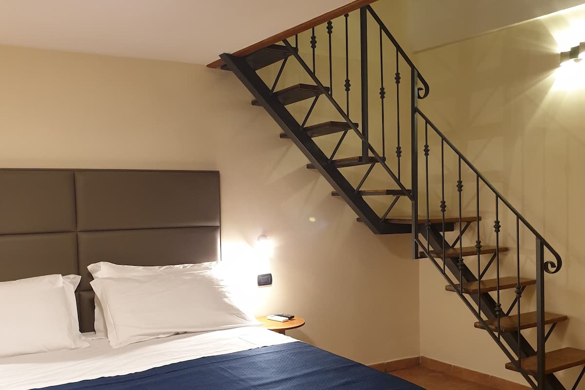 A bedroom with a bed, a nightstand, a wall-mounted light, and a staircase.
