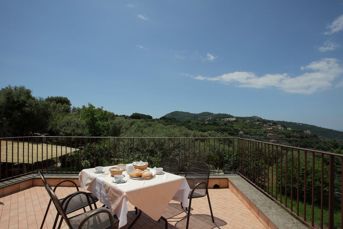 A terrace with a table set for dining, overlooking a scenic landscape with hills and a clear sky.
