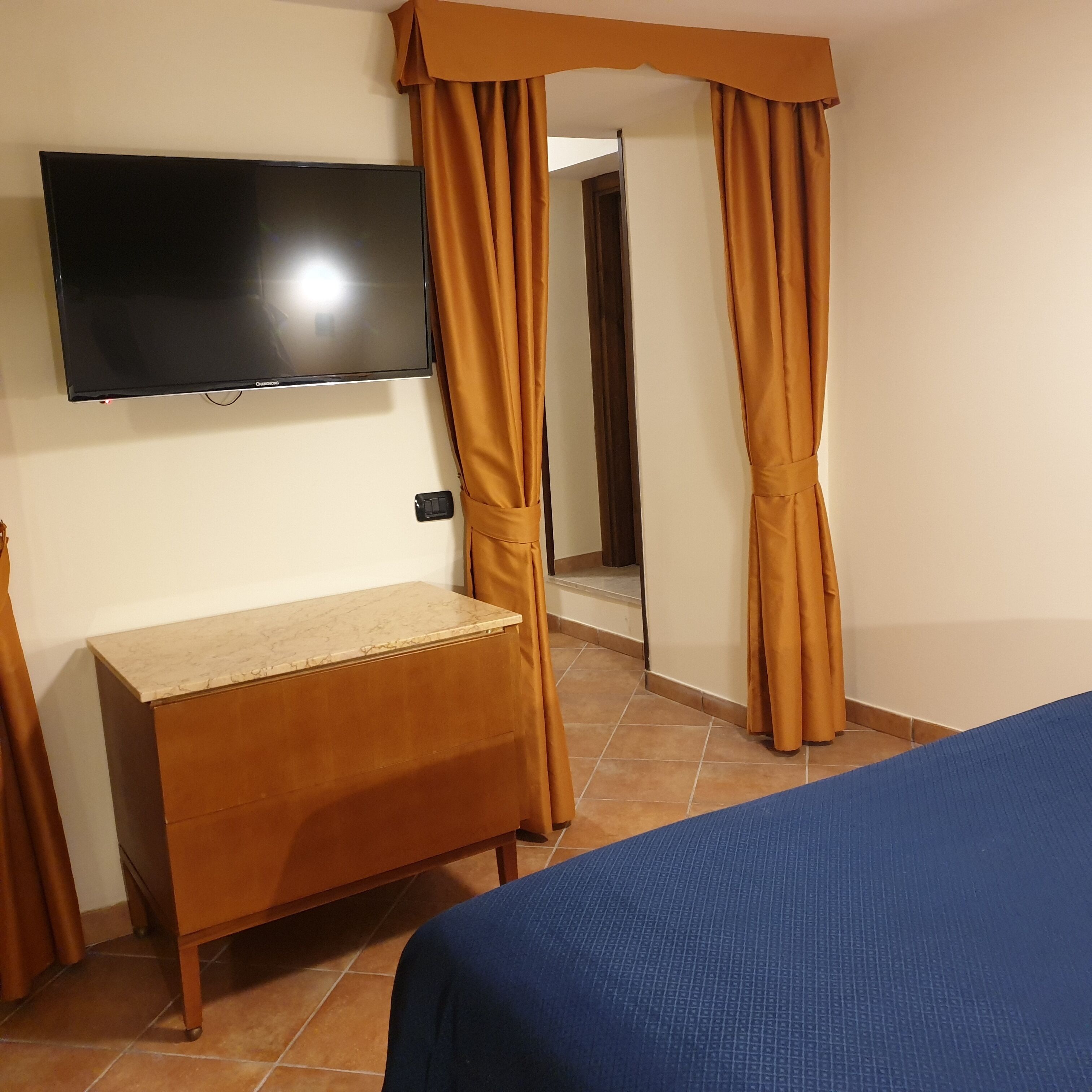 Une chambre avec un lit, un téléviseur fixé au mur, un bureau en bois et des rideaux.