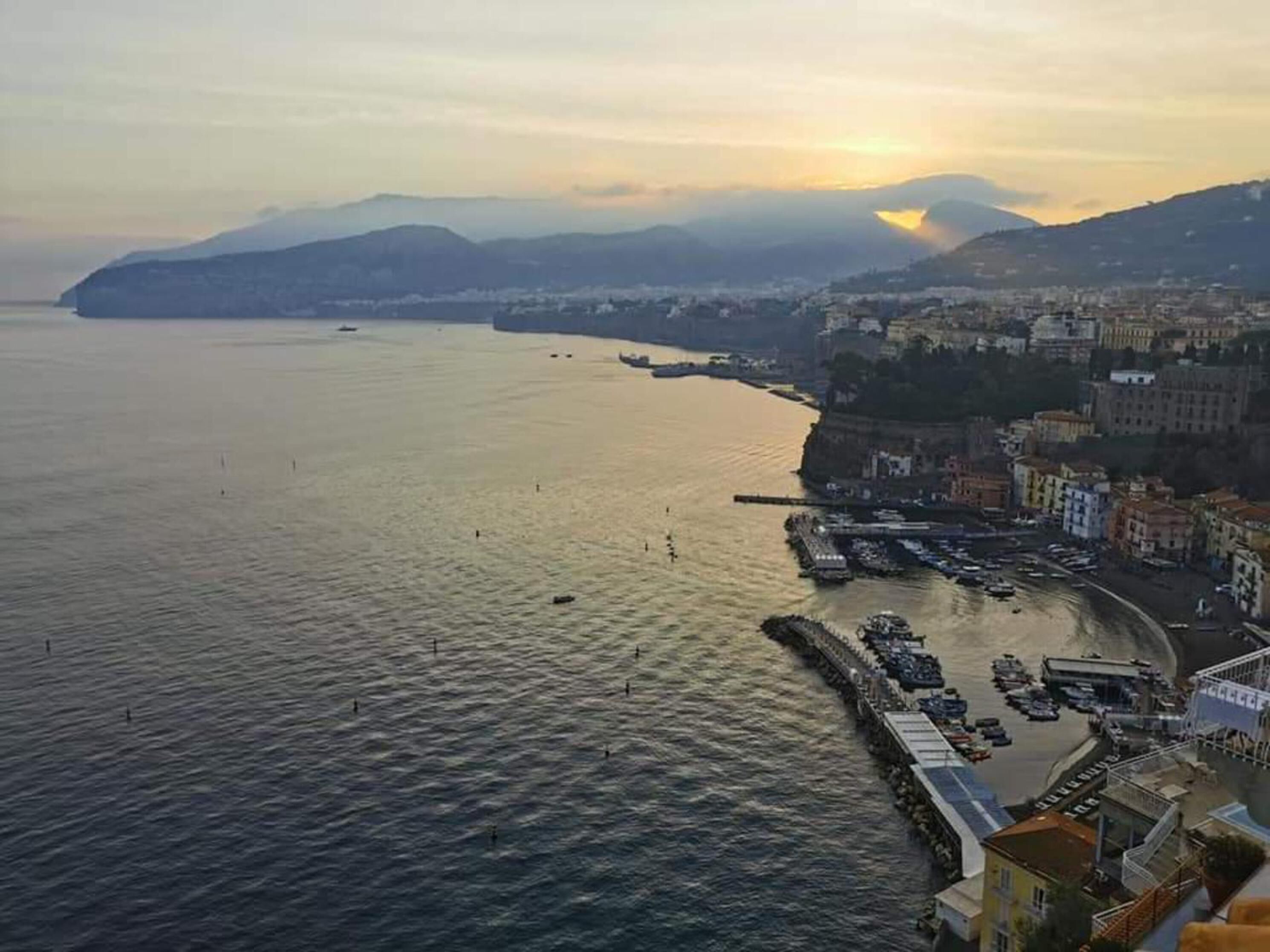 A coastal cityscape with a marina, buildings along the waterfront, and mountains in the background.