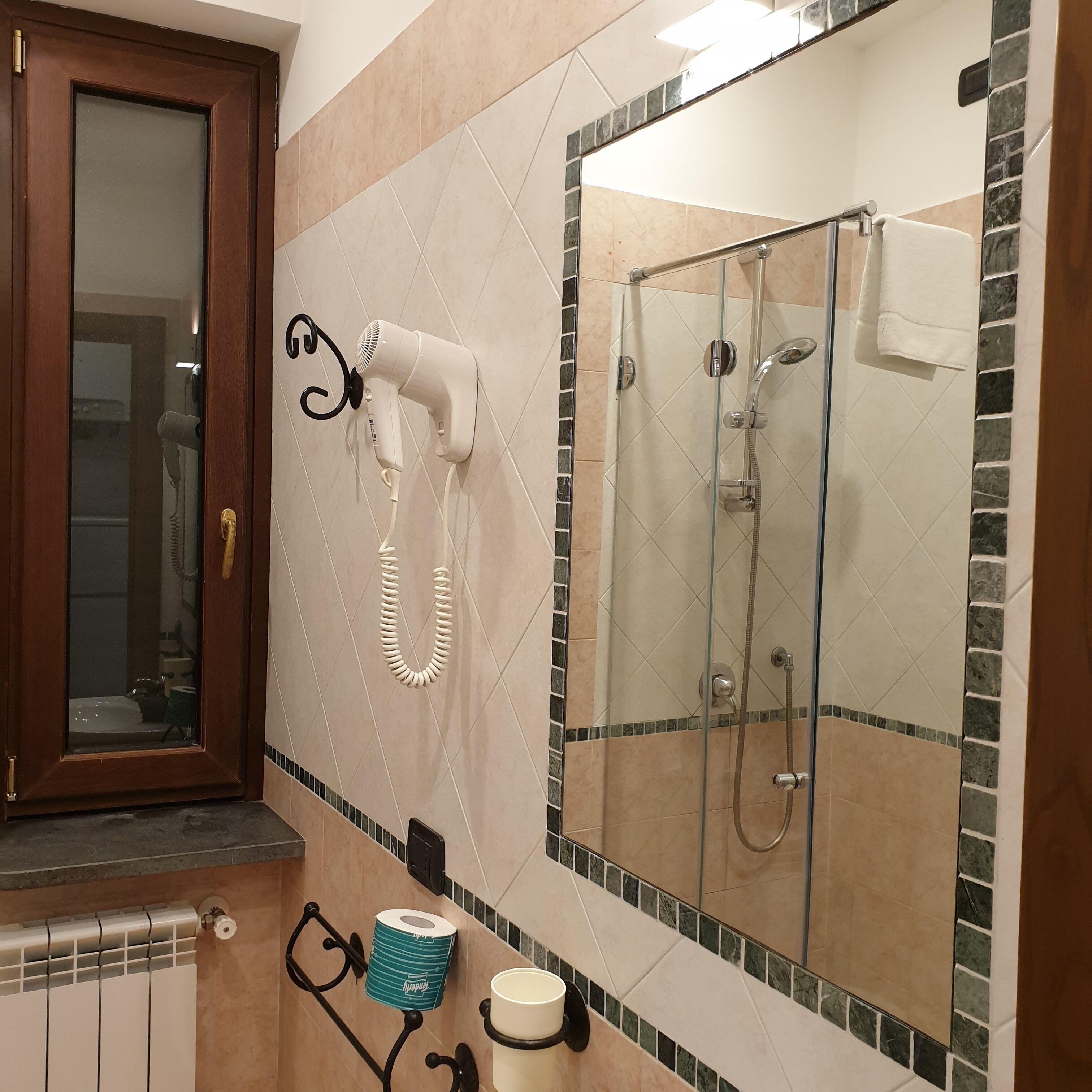 Un baño con un secador de pelo montado en la pared, cabina de ducha de vidrio y una toalla colgada en la puerta de la ducha.