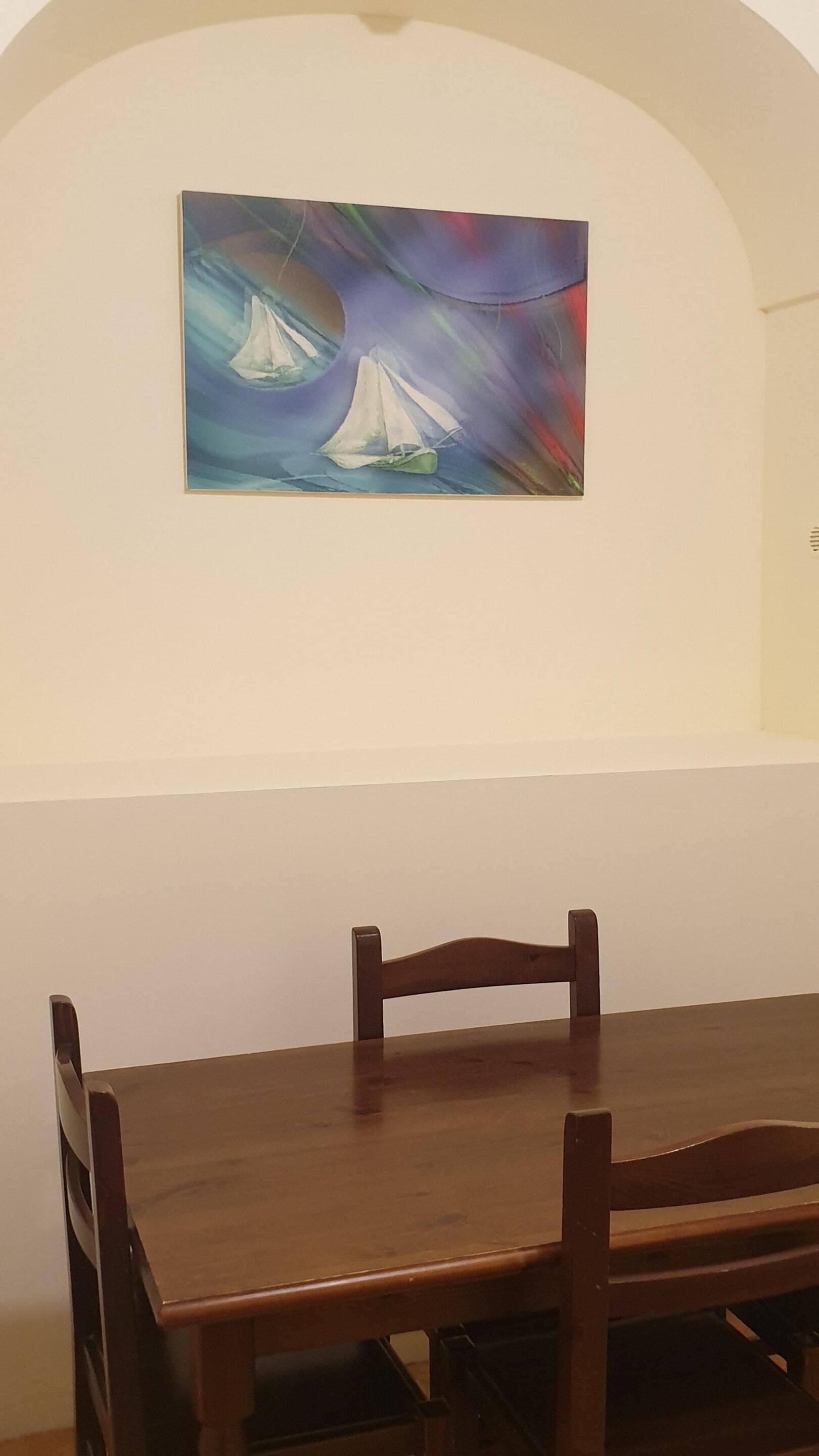 A dining area with a wooden table and chairs, a painting of sailboats on the wall, and a white ceiling.