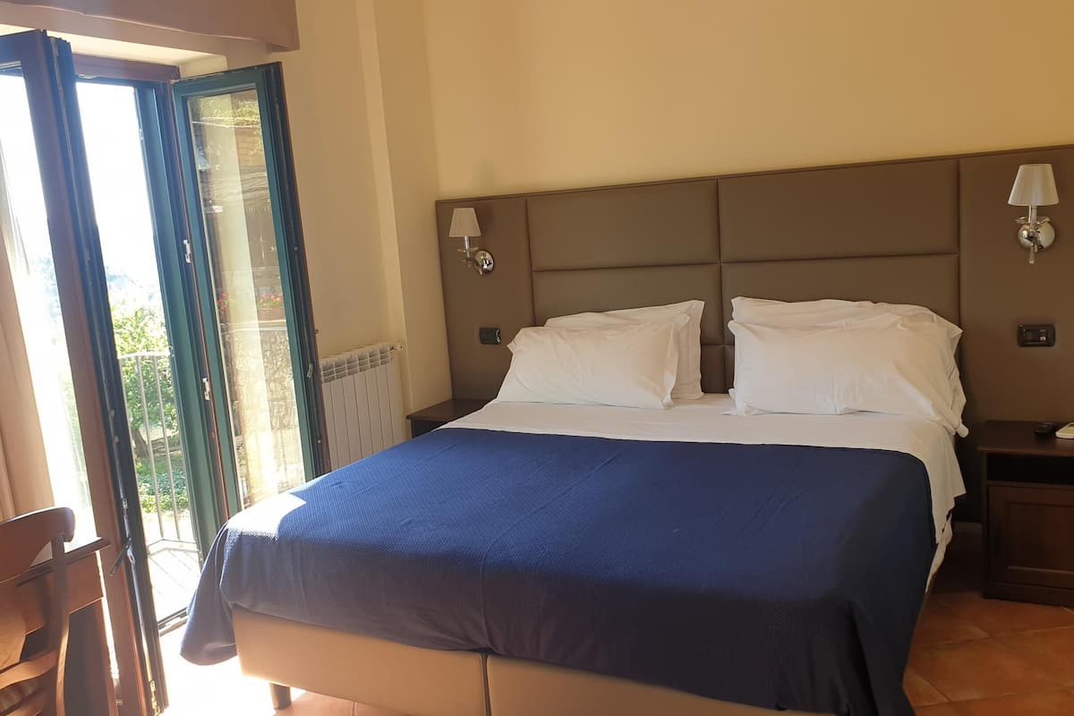 A hotel room with a bed, two bedside tables, a chair, and a view of the outdoors.