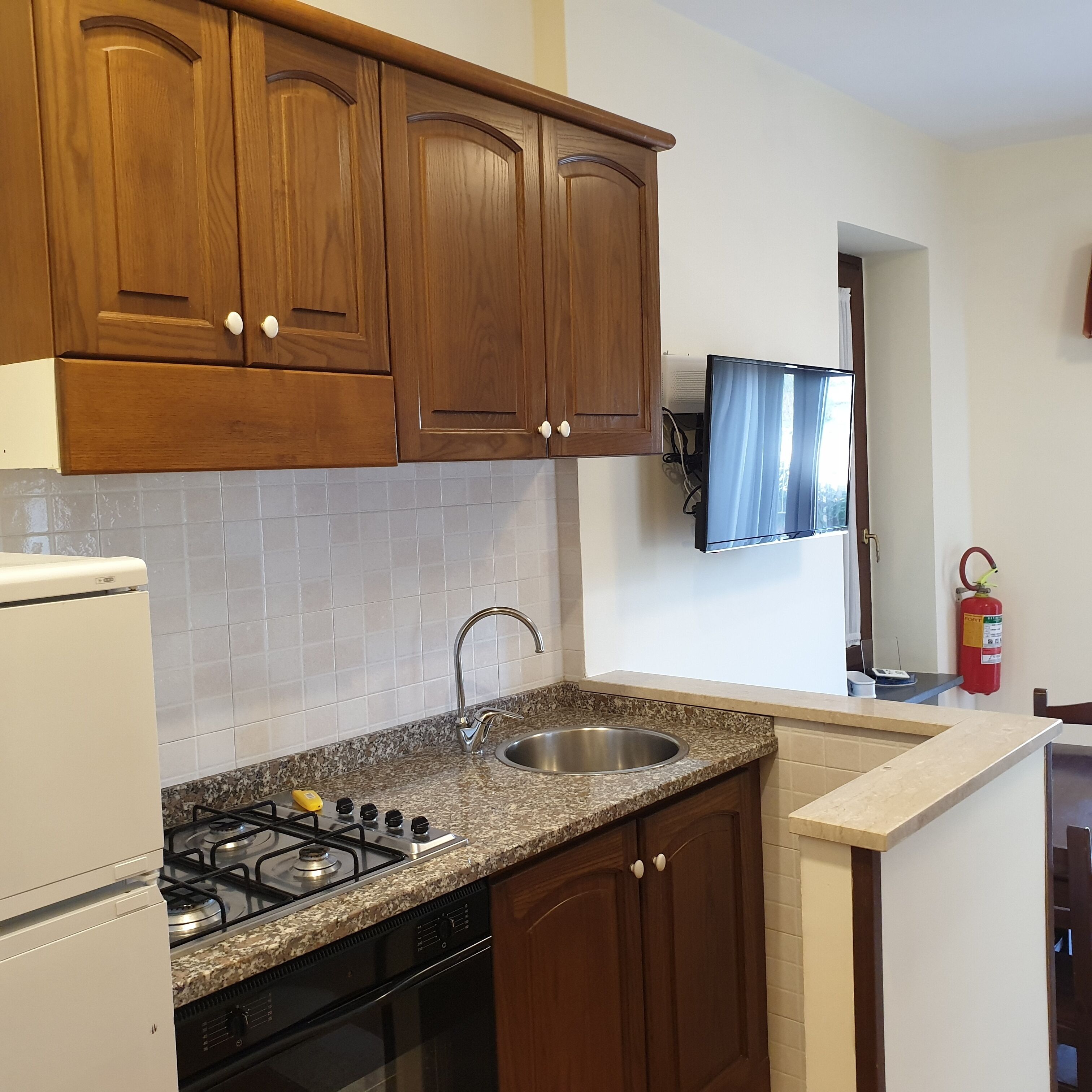 Eine Küche mit Holzausstattung, einer Arbeitsplatte aus Granit, einer Spüle aus Edelstahl, einem Gasherd und einem weißen Kühlschrank.