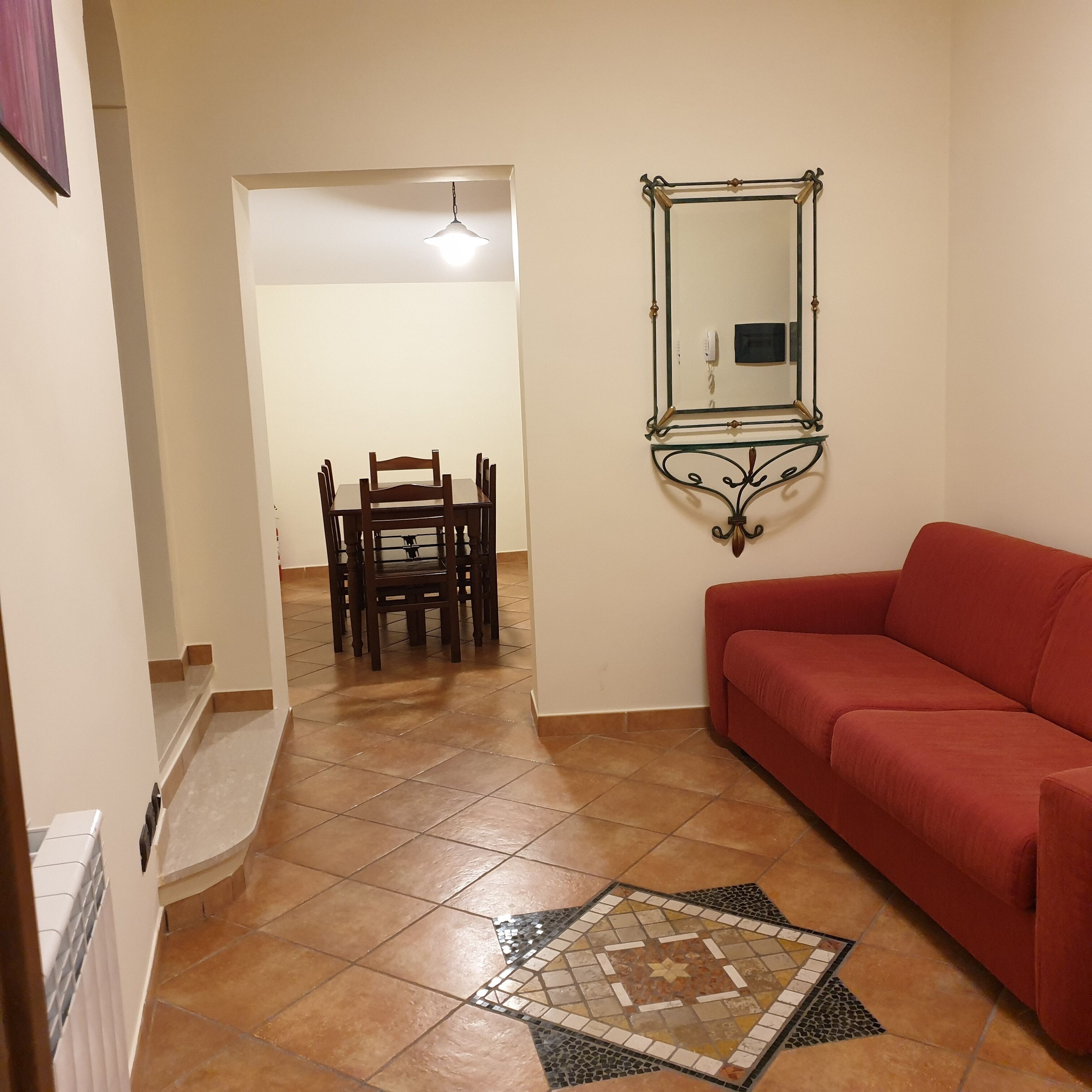 A living room with a red sofa, a dining area with a table and chairs, and a decorative mirror on the wall.
