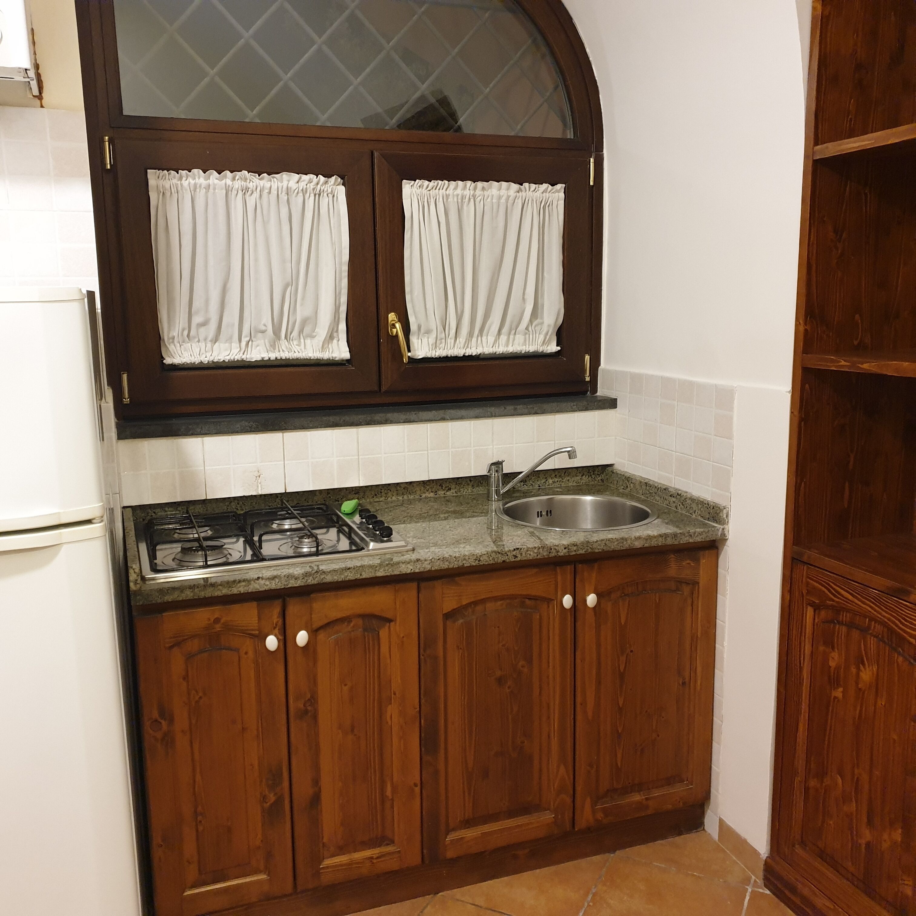 A kitchen with wooden cabinets, a gas stove, a sink, and a window with curtains.