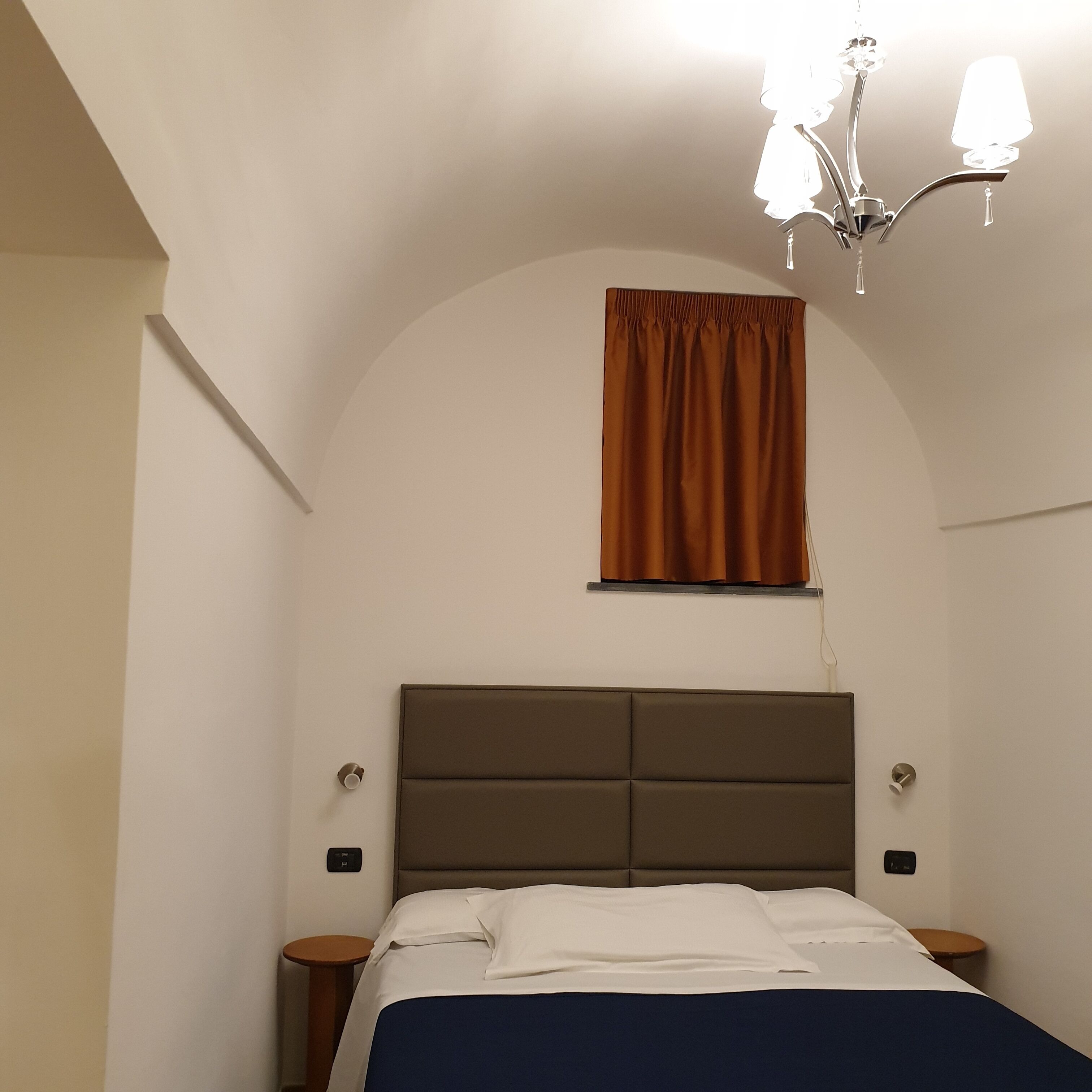 Un dormitorio con cama, una ventana con cortinas, un candelabro y mesitas de noche.