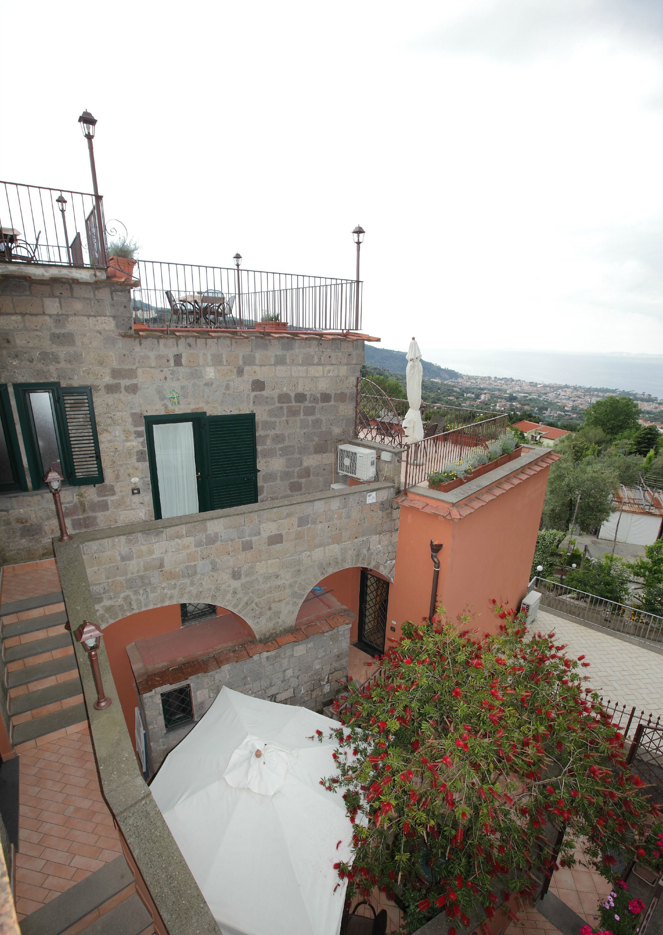 Une terrasse sur le toit offrant une vue sur la ville, un parasol blanc et une plante à fleurs rouges.