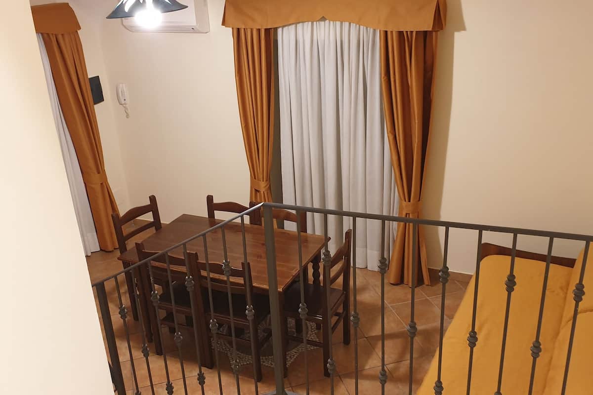 A dining area with a table and chairs, a staircase with a metal railing, and a window with curtains.