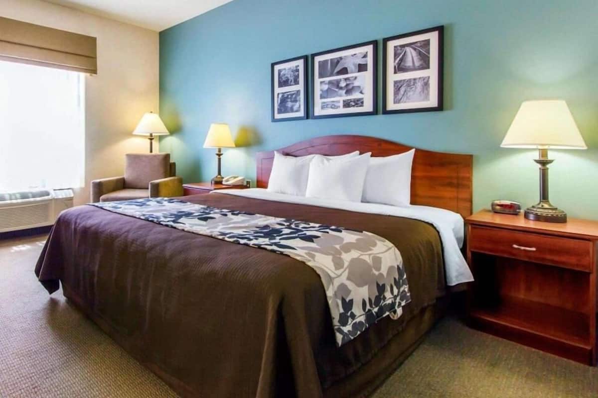 A hotel room with a bed, two bedside lamps, a nightstand, a window with blinds, and framed pictures on the wall.