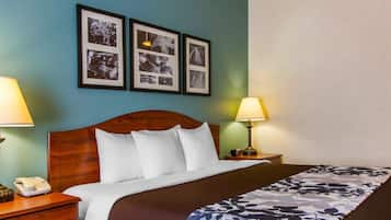 A hotel room with a wooden headboard, a bed with white bedding, two bedside lamps, a nightstand with a telephone, and a wall with framed pictures.