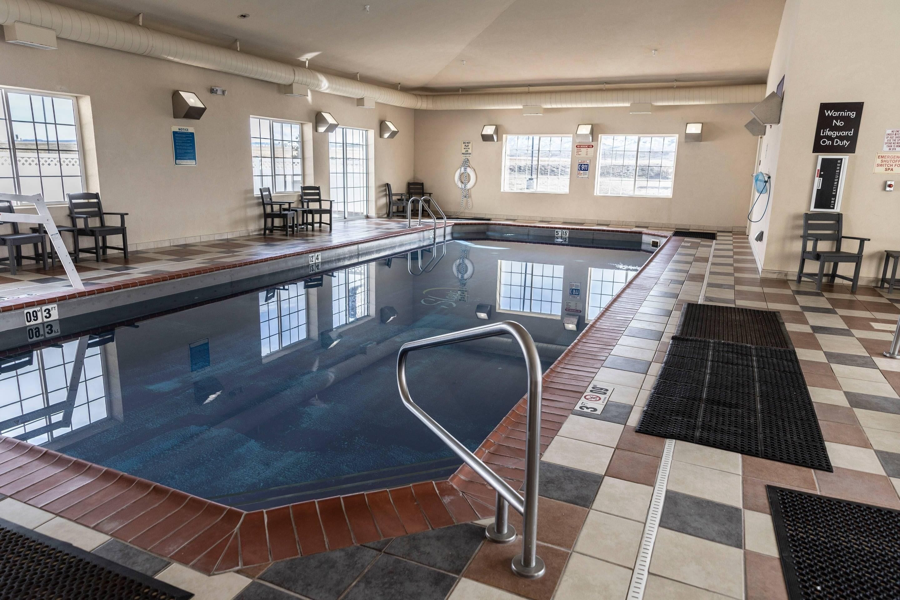 Una piscina interior con suelo de baldosas, una silla de salvavidas y una escalera de piscina.