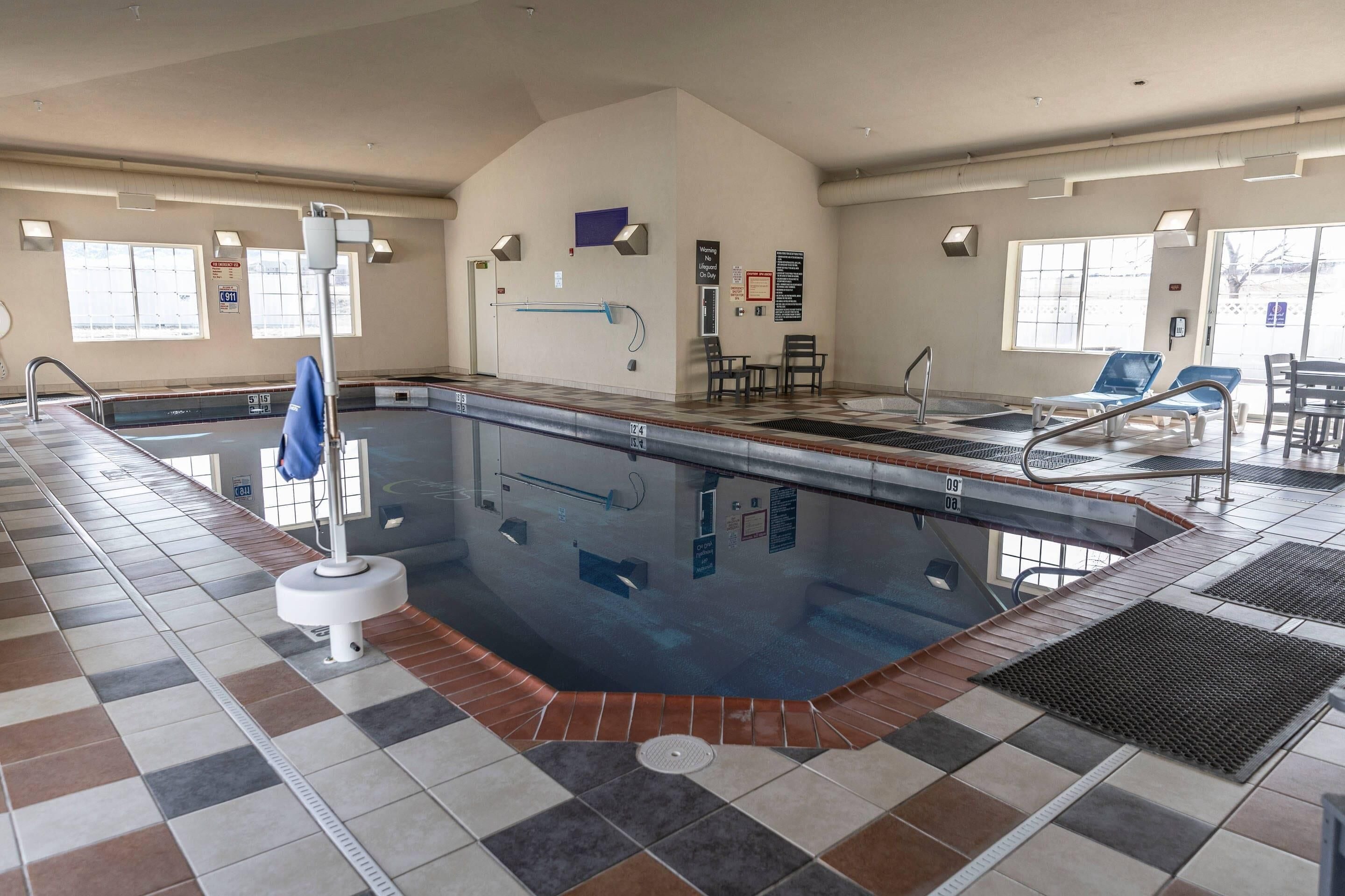 A swimming pool with a tiled floor, a blue lifeguard chair, and a water slide.