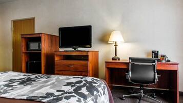 A hotel room with a bed, a desk with a chair, a television, a lamp, and a microwave.