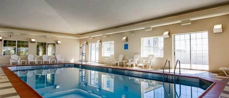 Une piscine intérieure à l’eau claire, entourée de chaises blanches et dotée d’un sol carrelé.