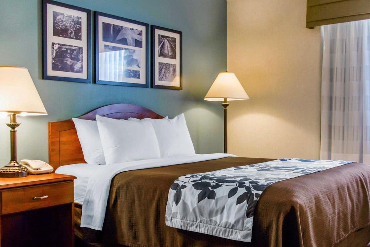 A hotel room with a bed, two bedside lamps, a nightstand with a phone, and three framed pictures on the wall.