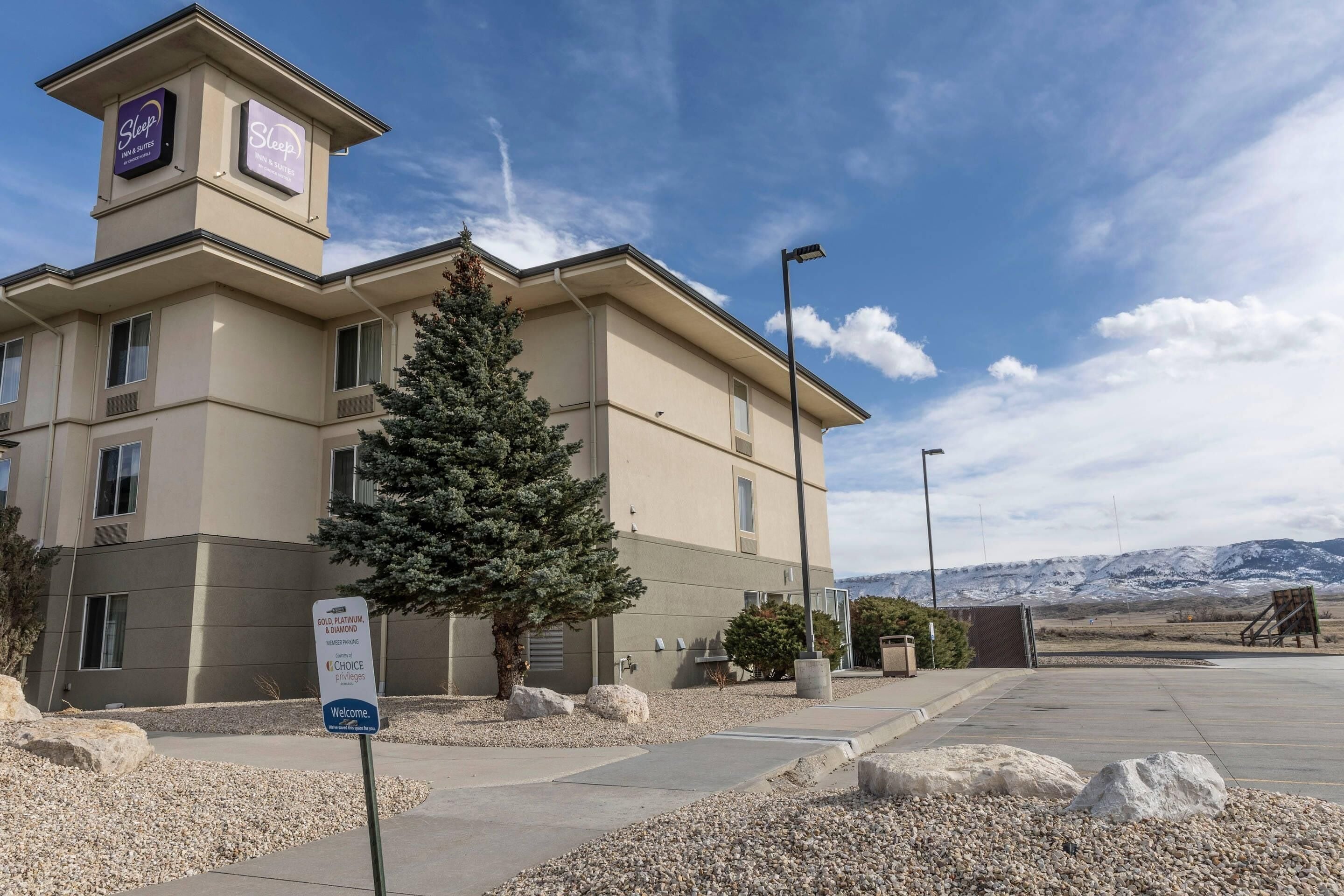 A hotel with a sign indicating 'Gold Platinum & Choice' accommodations, a welcoming sign, and a view of mountains in the background.