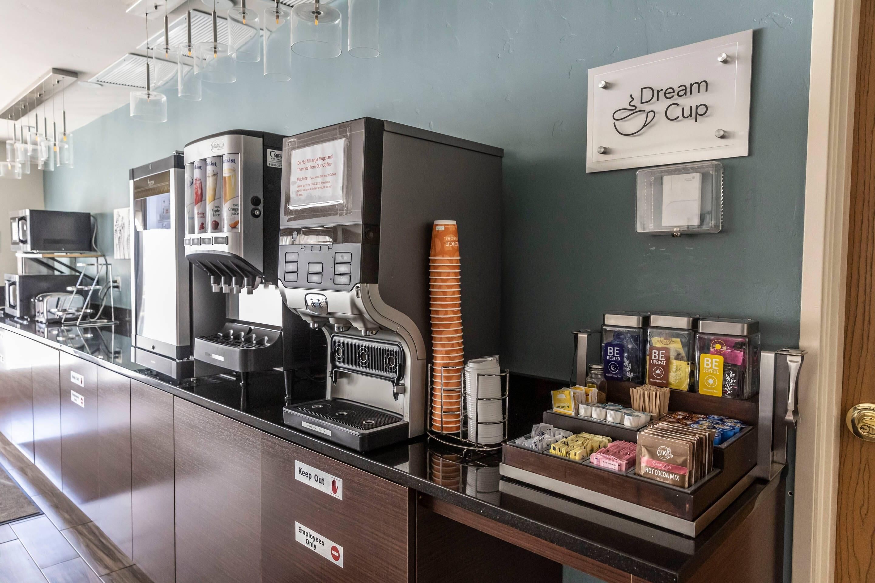 A coffee station with multiple coffee machines, a stack of disposable cups, and a variety of coffee pods and creamer packages.