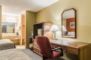 Habitación de hotel con un escritorio de madera, una silla roja, un espejo grande y una cama con colcha estampada.