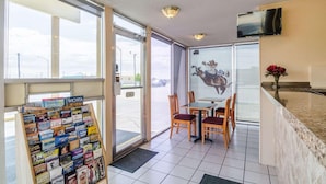 A hotel lobby with a travel book rack, a table with chairs, a TV mounted on the wall, and a large window offering a view of the street. - Executive Inn (Dodge City)