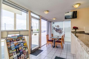 Un vestíbulo de hotel con un atril para libros de viaje, una mesa con sillas, un televisor montado en la pared y un gran ventanal con vistas a la calle.