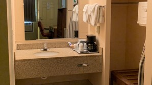 A bathroom with a sink, mirror, towel rack, and a coffee maker. - Executive Inn (Dodge City)