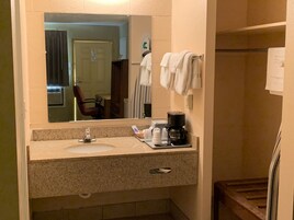 Un baño con lavamanos, espejo, toallero y cafetera.