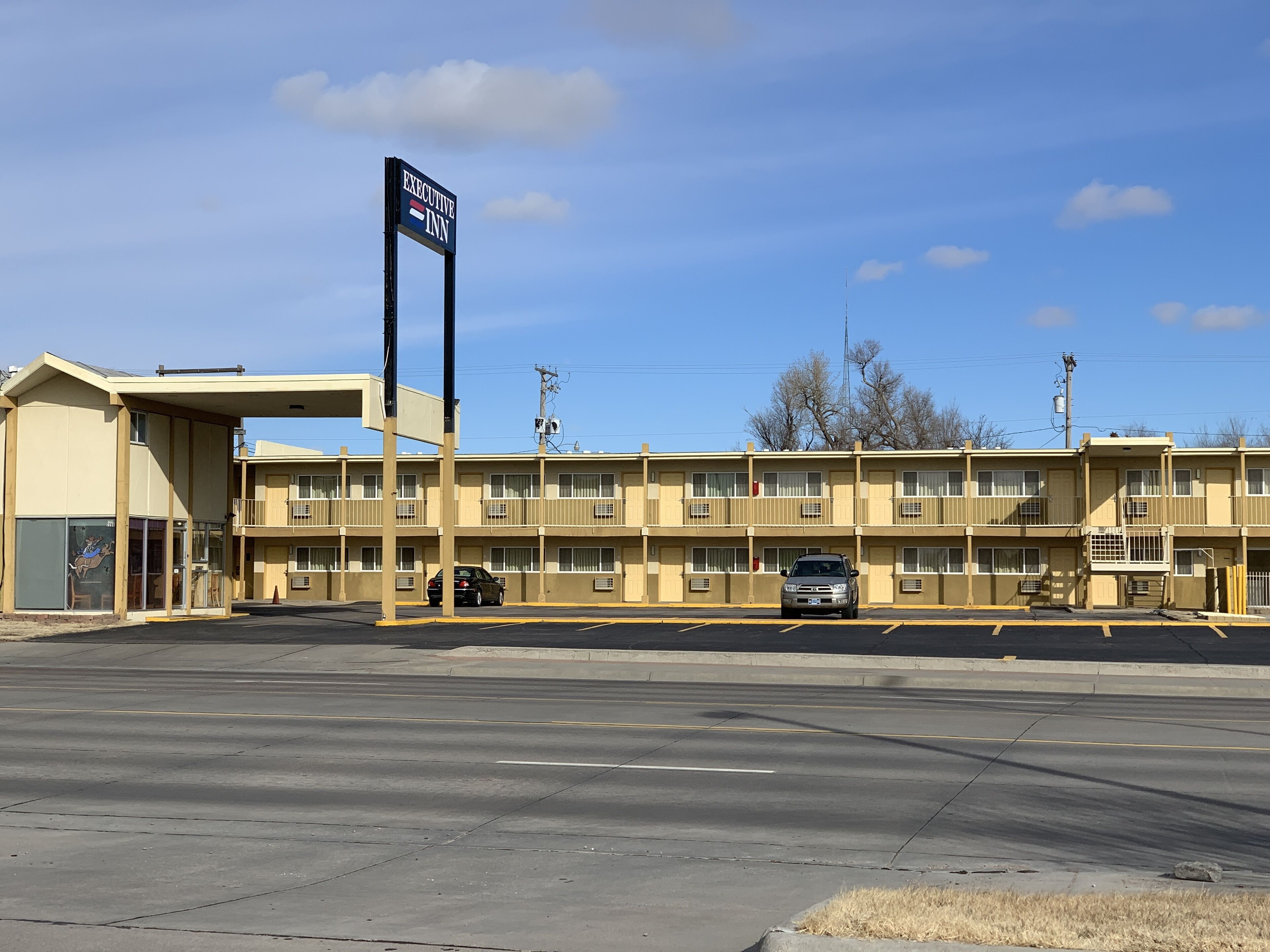Un motel con un letrero que dice 'EXECUTIVE INN' y un estacionamiento con dos coches.