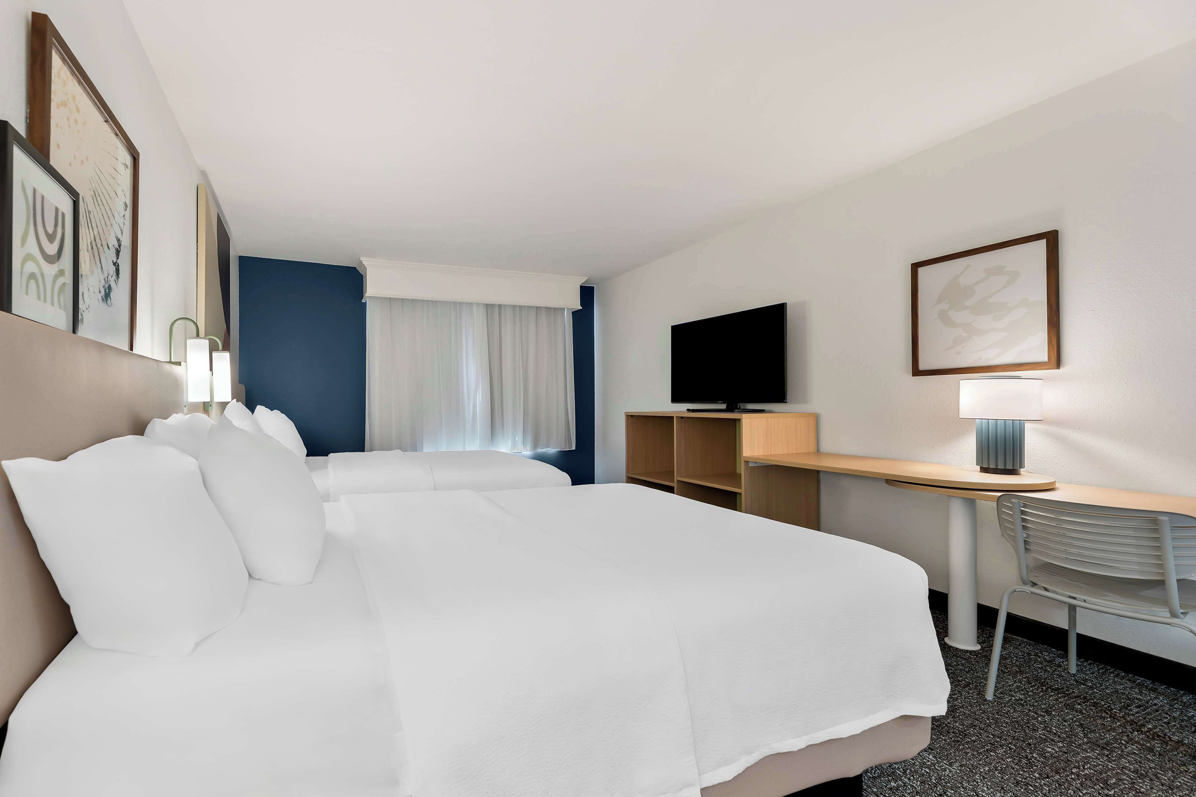 Habitación de hotel con una cama grande, un escritorio, una silla, un televisor y una ventana con cortinas.