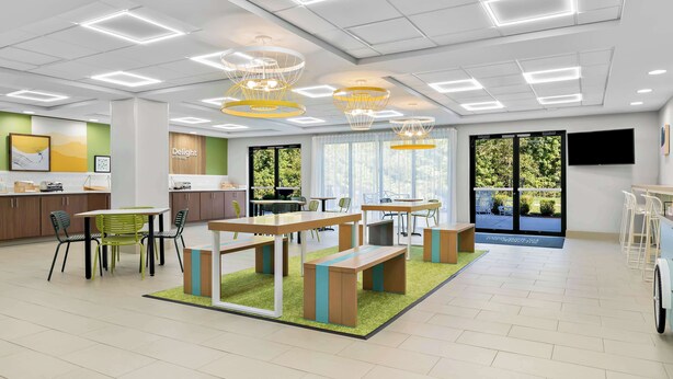 Un espacio de oficina moderno y bien iluminado, con varias mesas y sillas, una zona de recepción y ventanas amplias que dan a vistas de zonas verdes.
