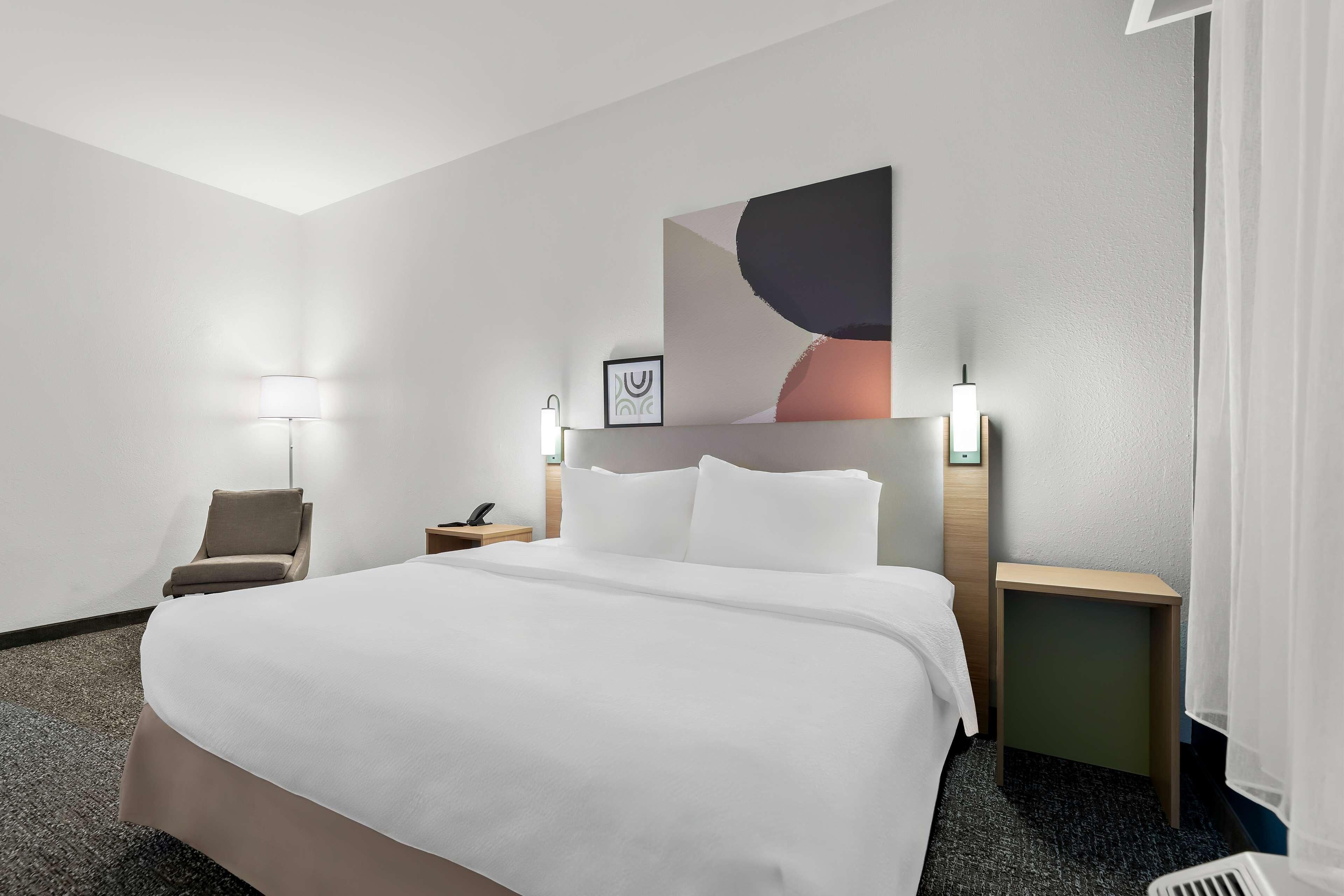 Een hotelkamer met een groot bed, een stoel, een nachtkastje, een lamp en een kunstwerk aan de muur.