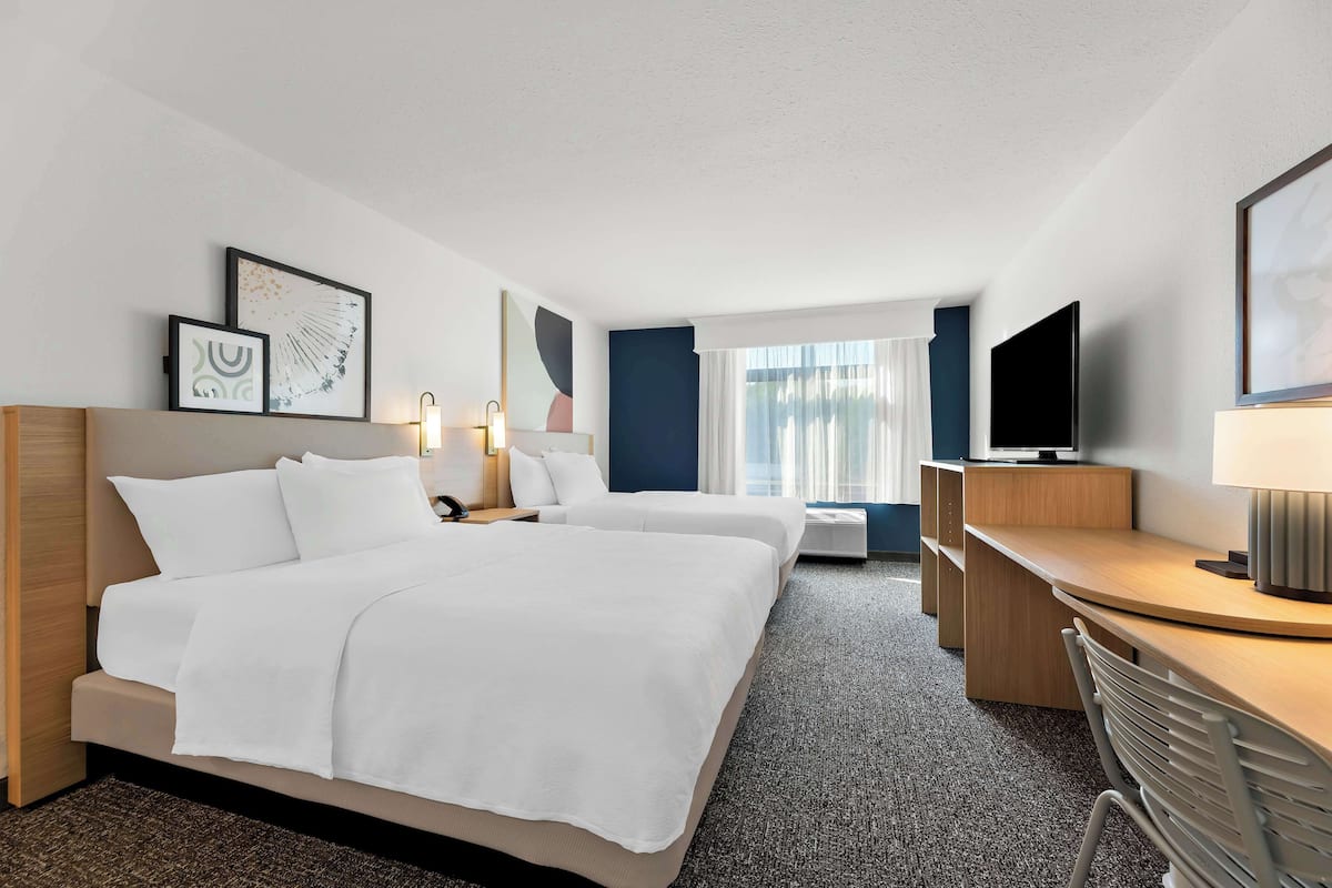 A hotel room with two beds, a desk, a TV, and artwork on the walls.