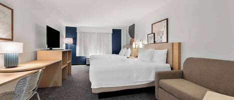 A hotel room with a bed, a desk, a chair, a sofa, a TV, and a window with curtains.
